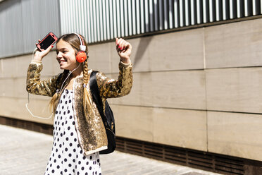 Lächelndes Mädchen mit Kopfhörern und Smartphone tanzt auf der Straße - ERRF00900