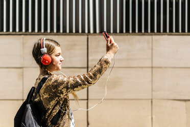 Mädchen mit Rucksack und Kopfhörern nimmt Selfie mit Smartphone - ERRF00901