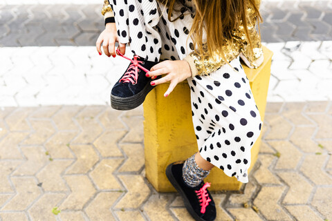 Mädchen sitzt auf Poller und bindet sich den Schuh, Teilansicht, lizenzfreies Stockfoto