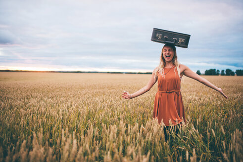 Woman balancing suitcase on head in wheat field, Edmonton, Canada - ISF21089