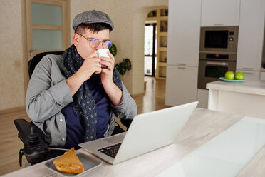 Physically impaired man drinking and working on laptop at home - CUF50326
