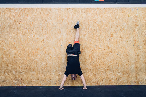 Man with disability doing handstand against chipboard wall - CUF50343