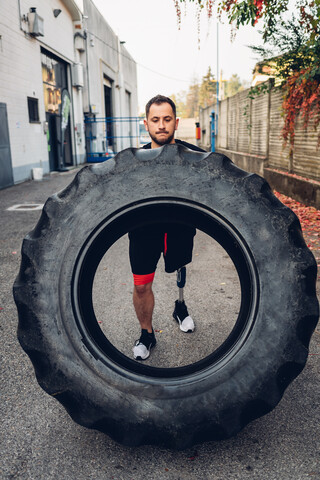 Mann mit Beinprothese macht Krafttraining mit Riesenreifen, lizenzfreies Stockfoto