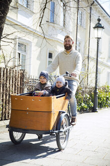 Glücklicher Vater mit zwei Kindern auf einem Lastenfahrrad in der Stadt - MAEF12832