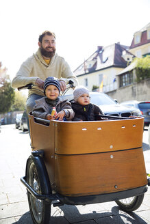 Glücklicher Vater mit zwei Kindern auf einem Lastenfahrrad in der Stadt - MAEF12833