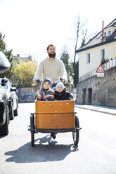 Glücklicher Vater mit zwei Kindern auf einem Lastenfahrrad in der Stadt - MAEF12834