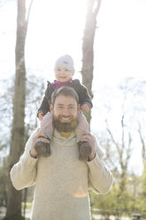 Portrait of happy father carrying daughter on shoulders in park - MAEF12843