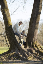 Father playing with son at a tree in park - MAEF12860