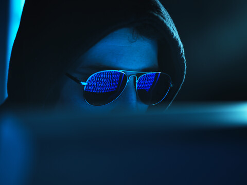 Cyberkriminalität, Spiegelung in der Brille eines Virus, der einen Computer hackt, Nahaufnahme des Gesichts, lizenzfreies Stockfoto