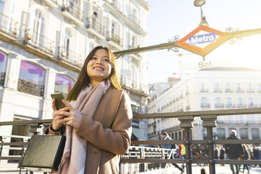 Spanien, Madrid, lächelnde junge Frau an der U-Bahn-Station Puerta del Sol mit Smartphone - WPEF01464
