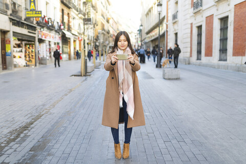 Spanien, Madrid, junge Frau, die in der Stadt Fotos mit einem Smartphone macht, lizenzfreies Stockfoto