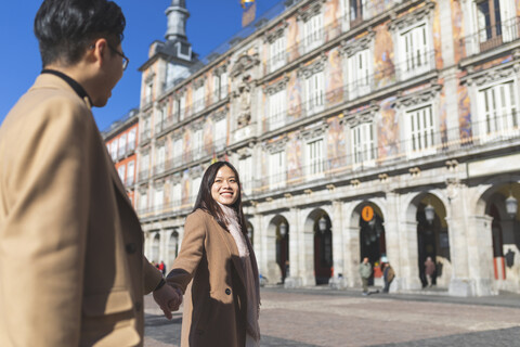 Spanien, Madrid, glückliches junges Touristenpaar, das auf der Plaza Mayor Händchen hält, lizenzfreies Stockfoto