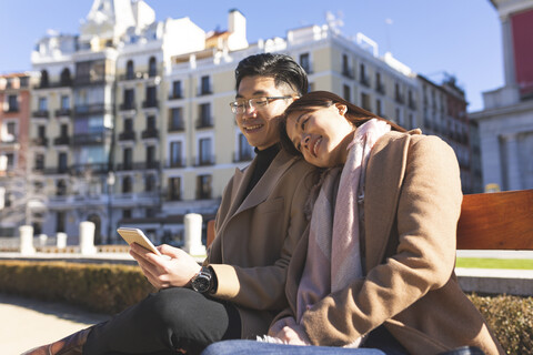 Spain, Madrid, young couple resting on a bench and using cell phone in the city stock photo