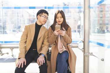 Spain, Madrid, young couple sitting at a station and using cell phone in the city - WPEF01501