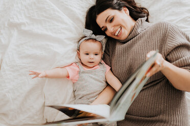 Mutter liest mit ihrer kleinen Tochter auf dem Bett - ISF21133