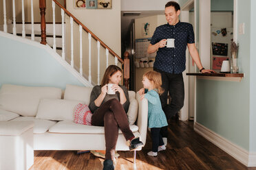 Mid adult couple having mug of coffee in living room with toddler daughter - ISF21160