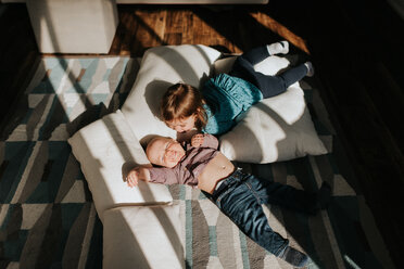 Baby boy and toddler sister lying on cushions on living room floor, overhead view - ISF21161