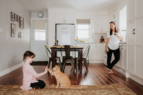 Mutter beobachtet Tochter spielen mit Katze zu Hause, lizenzfreies Stockfoto