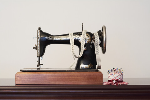 Alte Vintage-Nähmaschine mit Maßband und Stecknadeln in Form eines Hutes, lizenzfreies Stockfoto