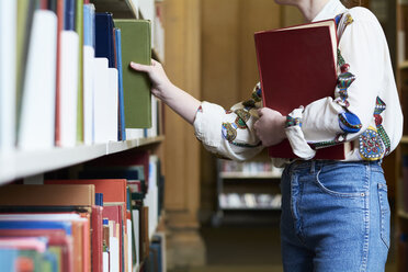 Studentin mit einem Buch in einer öffentlichen Bibliothek, die sich eines aussucht - IGGF01031
