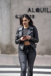 Young woman crossing the pedestrian crossing and using mobile phone - OCMF00385