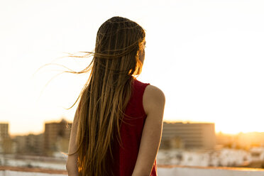 Rear view of teenage girl on roof terrace in the city at sunset - ERRF00960