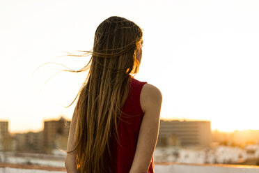 Rückansicht eines Teenagers auf einer Dachterrasse in der Stadt bei Sonnenuntergang - ERRF00960