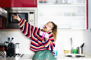 Mädchen spielt mit Mikrofon und Smartphone in der Küche zu Hause - ERRF00999
