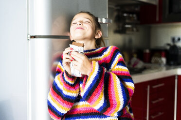 Mädchen im gestreiften Pullover in der Küche zu Hause beim Essen von Schokolade - ERRF01005