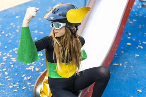 Mädchen im Superheldin-Kostüm auf Spielplatzrutsche beim Anspannen der Muskeln - ERRF01024