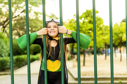 Glückliches Mädchen im Superheldenkostüm hinter Gittern, lizenzfreies Stockfoto