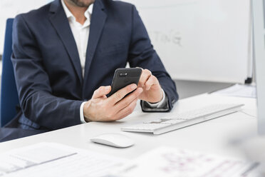 Nahaufnahme eines Geschäftsmannes, der an einem Schreibtisch im Büro sitzt und ein Mobiltelefon benutzt - MGIF00373