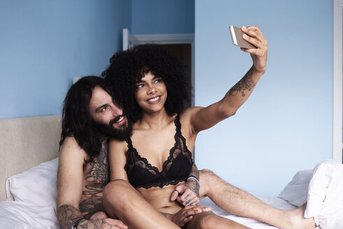 Glückliches zärtliches junges Paar, das ein Selfie im Bett macht - IGGF01068