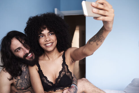 Glückliches zärtliches junges Paar, das ein Selfie im Bett macht - IGGF01070