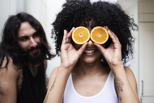 Glückliche junge Frau, die ihre Augen mit Orangen in der Küche bedeckt - IGGF01078