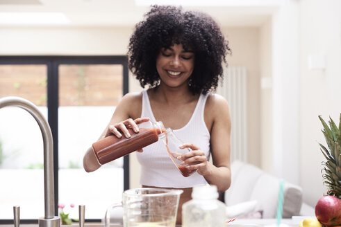 Smiling young woman preparing healthy smoothie in kitchen - IGGF01092