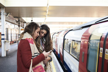 UK, London, zwei Frauen telefonieren auf dem Bahnsteig einer U-Bahn-Station - IGGF01103