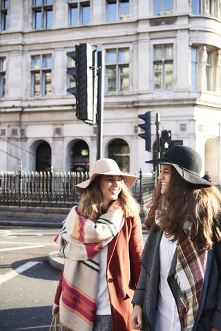 UK, London, zwei glückliche Frauen in der Stadt, die eine Straße überqueren, lizenzfreies Stockfoto