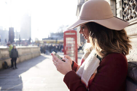 UK, London, Frau in der Stadt, die einen Schlapphut trägt und ein Mobiltelefon benutzt, lizenzfreies Stockfoto