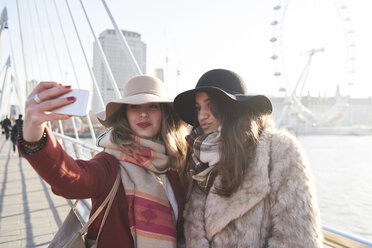 UK, London, zwei Frauen machen ein Selfie auf der Millennium Bridge mit dem London Eye im Hintergrund - IGGF01135
