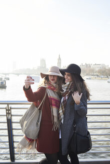 UK, London, zwei Frauen machen ein Selfie auf der Millennium Bridge mit Stadtbild im Hintergrund - IGGF01137