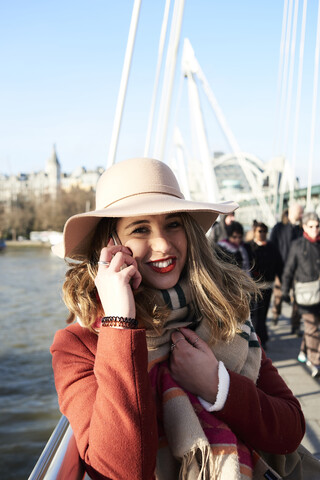 UK, London, stilvolle junge Frau, die auf der Millennium Bridge mit einem Handy telefoniert, lizenzfreies Stockfoto