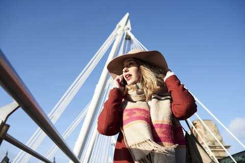 UK, London, stilvolle junge Frau, die auf der Millennium Bridge mit einem Handy telefoniert, lizenzfreies Stockfoto