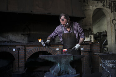 Schmied bei der Arbeit mit dem Hammer am Amboss in seiner Werkstatt - ABZF02295