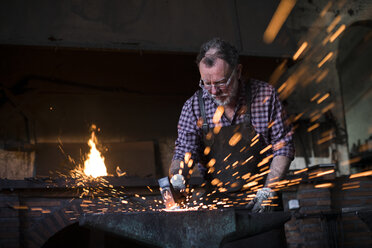 Schmied bei der Arbeit mit dem Hammer am Amboss in seiner Werkstatt - ABZF02301