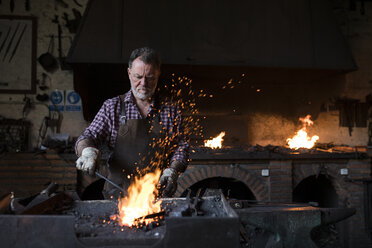 Blacksmith working at forge in his workshop - ABZF02309