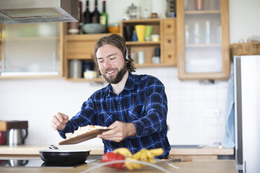 Junger Mann mit Bart, kariertem Hemd und Headset, der in der Küche Gemüse kocht - SGF02364