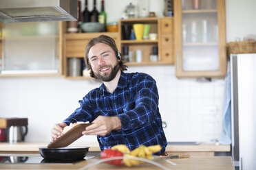 Young man with beard and plaid shirt, and headset cooking vegetables in kitchen - SGF02365