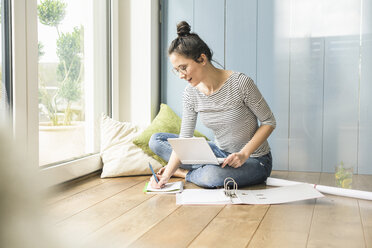 Woman sitting at the window at home taking notes - UUF17166