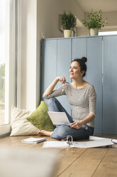 Lächelnde Frau, die zu Hause am Fenster sitzt und mit Laptop und Aktenordner arbeitet - UUF17168